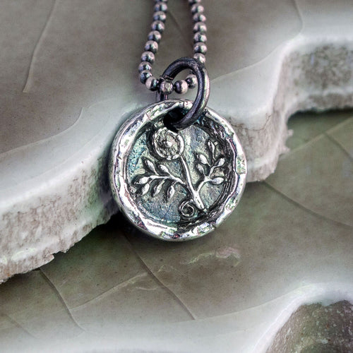 A silver flower pendant necklace with a vintage design, featuring a morning glory flower motif, displayed on a textured background.