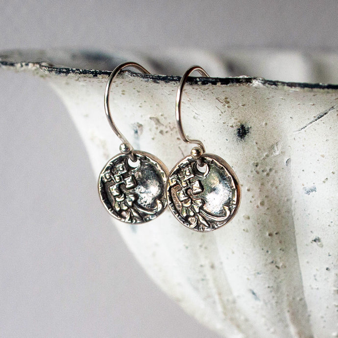 Silver earrings with intricate designs on a textured surface