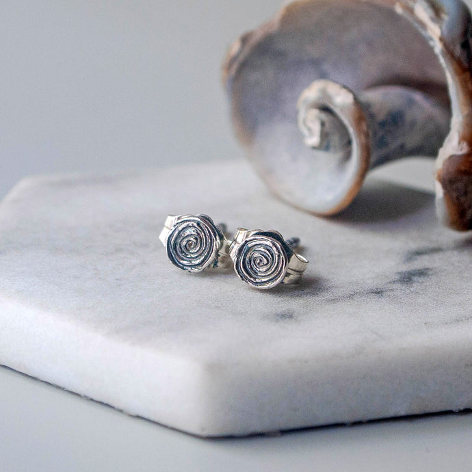 Silver spiral stud earrings on a marble surface with a shell in the background.