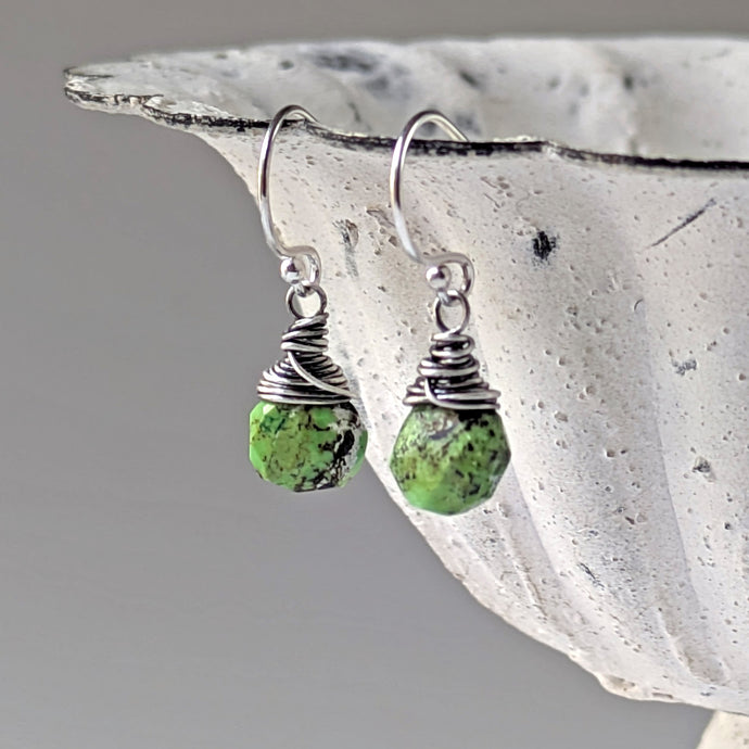 Green stone earrings with silver wire wrapping dangle from a decorative bowl