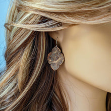 Load image into Gallery viewer, Close-up of a person wearing ornate earrings with a neutral background
