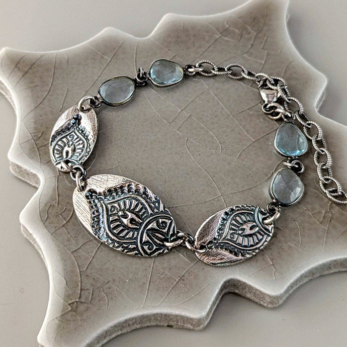 Silver bracelet with leaf-shaped charms and aquamarine stones on a textured beige surface