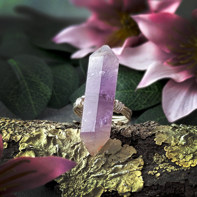 Amethyst crystal ring on a branch with pink flowers in the background