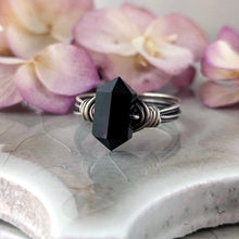 Load image into Gallery viewer, A double point onyx and silver ring sits on a ceramic beige tile with blurred flowers.
