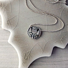 Load image into Gallery viewer, Silver necklace with a detailed floral pendant on a textured surface
