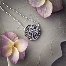 Load image into Gallery viewer, Silver necklace with a decorative floral pendant on a textured surface with flowers.
