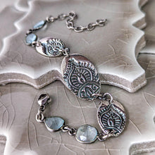 Load image into Gallery viewer, Silver bracelet with decorative elements and gemstones on a textured surface
