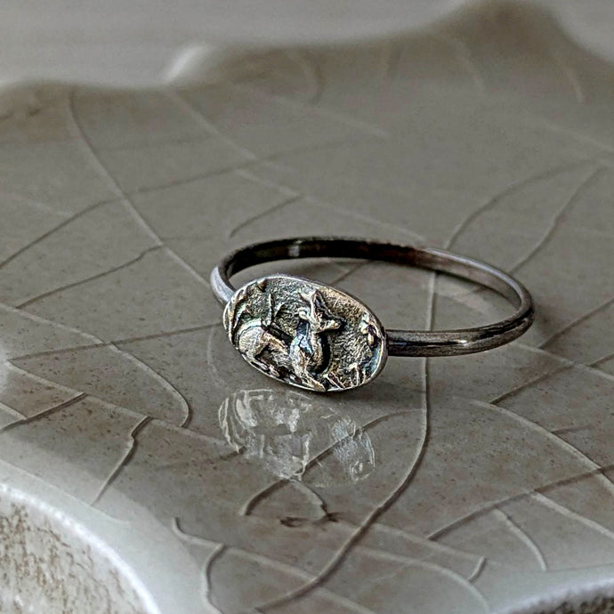 Silver ring with a detailed design on a textured ceramic surface