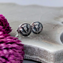 Load image into Gallery viewer, Silver earrings with floral design on a textured surface with purple flowers.
