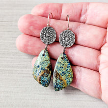 Load image into Gallery viewer, Pair of earrings with floral designs and teardrop-shaped stones held between fingers on a neutral background

