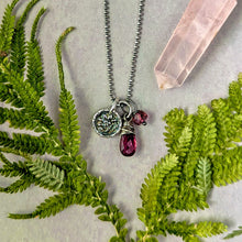 Load image into Gallery viewer, Necklace with charms on a surface with green leaves and a crystal.
