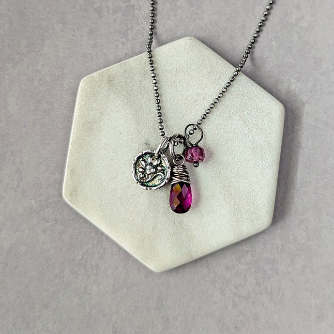 Necklace with charms on a hexagonal white stand against a gray background