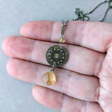 Load image into Gallery viewer, Necklace with a decorative pendant with a yellow stone drop held in a hand against a neutral background
