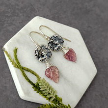 Load image into Gallery viewer, Silver earrings with pink leaf-like stones on a hexagonal stone surface with greenery.
