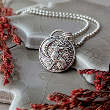 Load image into Gallery viewer, Silver pendant necklace crescent moon and hare imagery on a textured surface with red dried flowers
