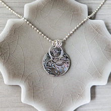 Load image into Gallery viewer, Silver necklace with a detailed pendant back view on a textured ceramic surface
