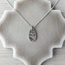 Load image into Gallery viewer, Back of pendant on a textured stone surface
