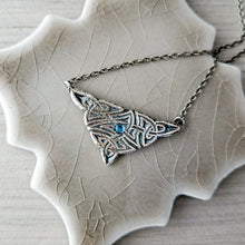 Load image into Gallery viewer, Silver necklace with a triangular pendant and blue gemstone on a textured beige surface
