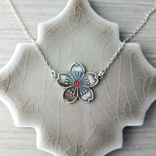Load image into Gallery viewer, Silver floral pendant with red gemstone necklace on a textured ceramic stand
