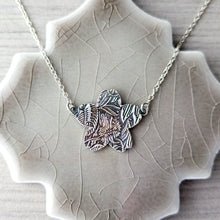 Load image into Gallery viewer, Reverse side of necklace with a detailed floral texture on a textured ceramic surface

