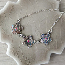 Load image into Gallery viewer, Silver necklace with floral pendants with rubies on a textured ceramic surface
