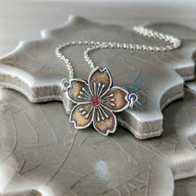 Load image into Gallery viewer, Silver floral pendant with red gemstone necklace on a textured ceramic stand

