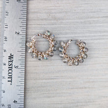 Load image into Gallery viewer, A pair of handmade hoop earrings with silver wire wrapping and grayish beige faceted stones with iridescent blue flashes, displayed next to a ruler for scale
