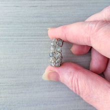 Load image into Gallery viewer, A close-up of a hand holding a pair of hoop earrings with round gray stones, set against a gray wood-grain background.
