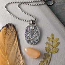 Load image into Gallery viewer, A silver necklace with an intricately designed pendant depicting a flying bat with a pale gray stone laying on a crackle glazed beige tile with a feather, an orange stone, and a leaf
