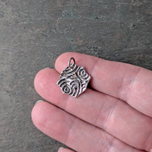 Load image into Gallery viewer, The reverse side of the spider pendant with a concentric repeating circular pattern held in a person's hand to show size
