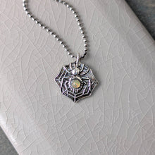 Load image into Gallery viewer, A silver spider with a smooth opal stone set into the abdomen laying flat on a crackle glazed beige tile
