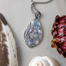 Load image into Gallery viewer, A teardrop shaped silver pendant with a green faceted stone laying flat on a crackle glazed beige tile with a feather, a shell, and a dried flower

