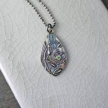 Load image into Gallery viewer, A teardrop shaped silver pendant with a green faceted stone lying flat on a white crackle glazed tile
