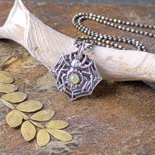 Load image into Gallery viewer, A silver spider with a smooth opal stone set into the abdomen rests against a fossilized shell fragment on a stone tile with a leaf
