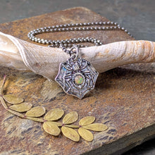 Load image into Gallery viewer, A silver spider with a smooth opal stone set into the abdomen propped up against a fossilized shell fragment on a stone tile with a dried leaf
