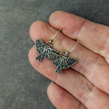 Load image into Gallery viewer, Silver Luna moth earrings held between fingers against a gray background
