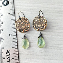 Load image into Gallery viewer, A pair of handmade dangle earrings displayed next to a metal ruler for scale. The earrings feature an antique bronze lotus flower disc with a faceted light green teardrop gemstone dangling below, wrapped in dark silver wire.
