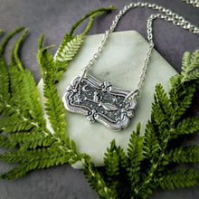 Load image into Gallery viewer, Silver necklace with a decorative pendant on a stone surface surrounded by green ferns
