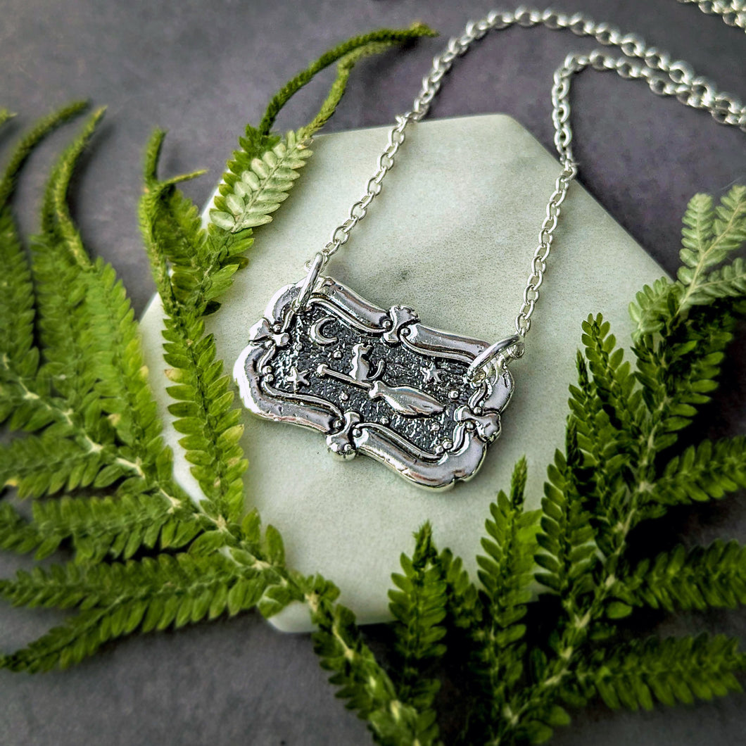 Silver necklace with a decorative pendant on a stone surface surrounded by green ferns