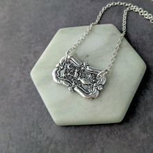 Load image into Gallery viewer, Silver necklace with an ornate pendant on a white stone surface
