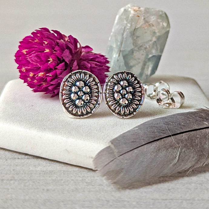 Silver earrings with floral design on a white surface with a pink flower and crystal in the background.