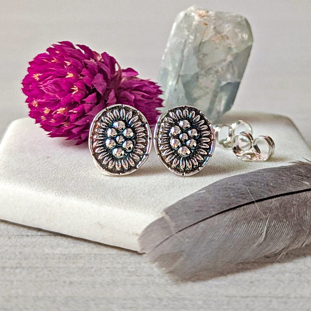 Silver earrings with floral design on a white surface with a pink flower and crystal in the background.