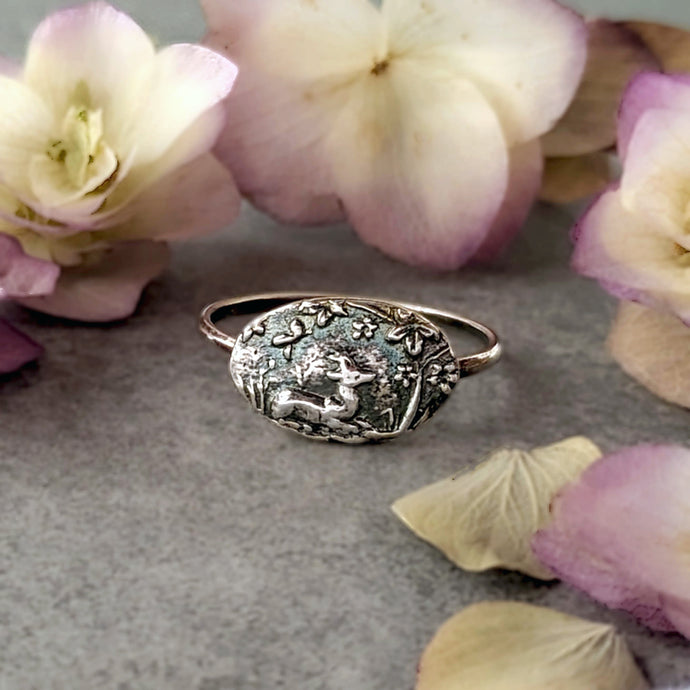 Silver ring with intricate design on a gray surface with flowers