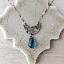 Load image into Gallery viewer, Silver crescent moon pendant with blue teardrop gemstone on a textured beige surface
