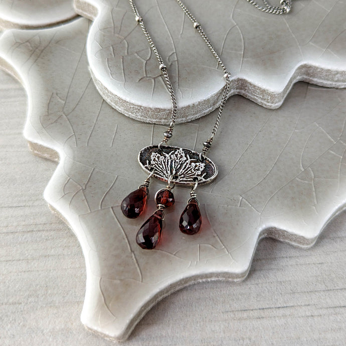 Silver necklace with red teardrop beads on a ceramic surface