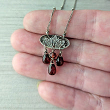 Load image into Gallery viewer, Silver necklace with floral design and teardrop garnets held in a hand for scale
