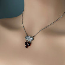 Load image into Gallery viewer, Necklace with a detailed oval pendant and garnet beads on a mannequin neck against a blue background
