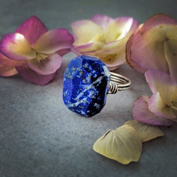 Blue lapis lazuli stone ring on a gray surface with pink and yellow flowers