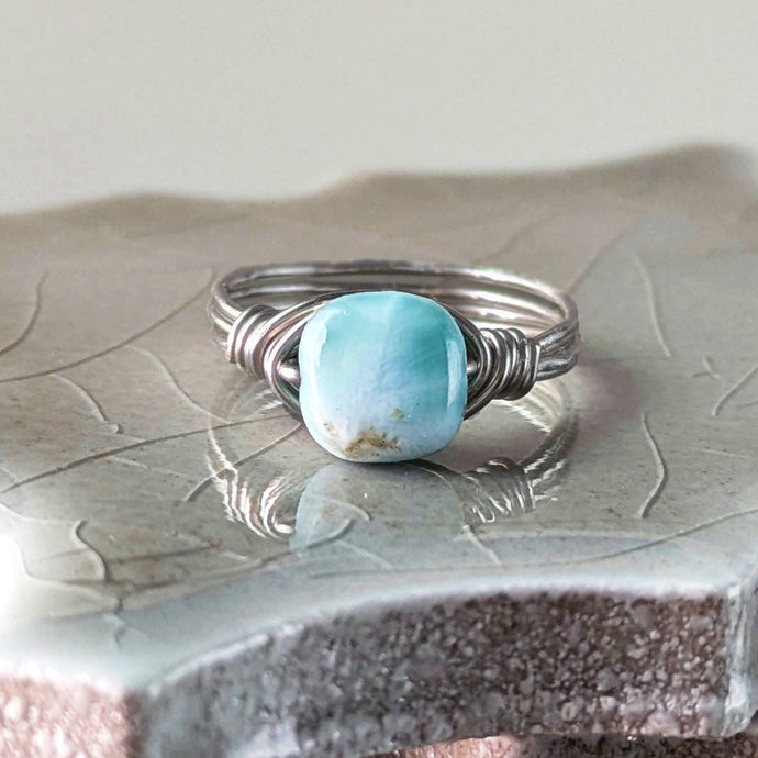 Silver ring with a square shaped light blue larimar stone on a textured surface