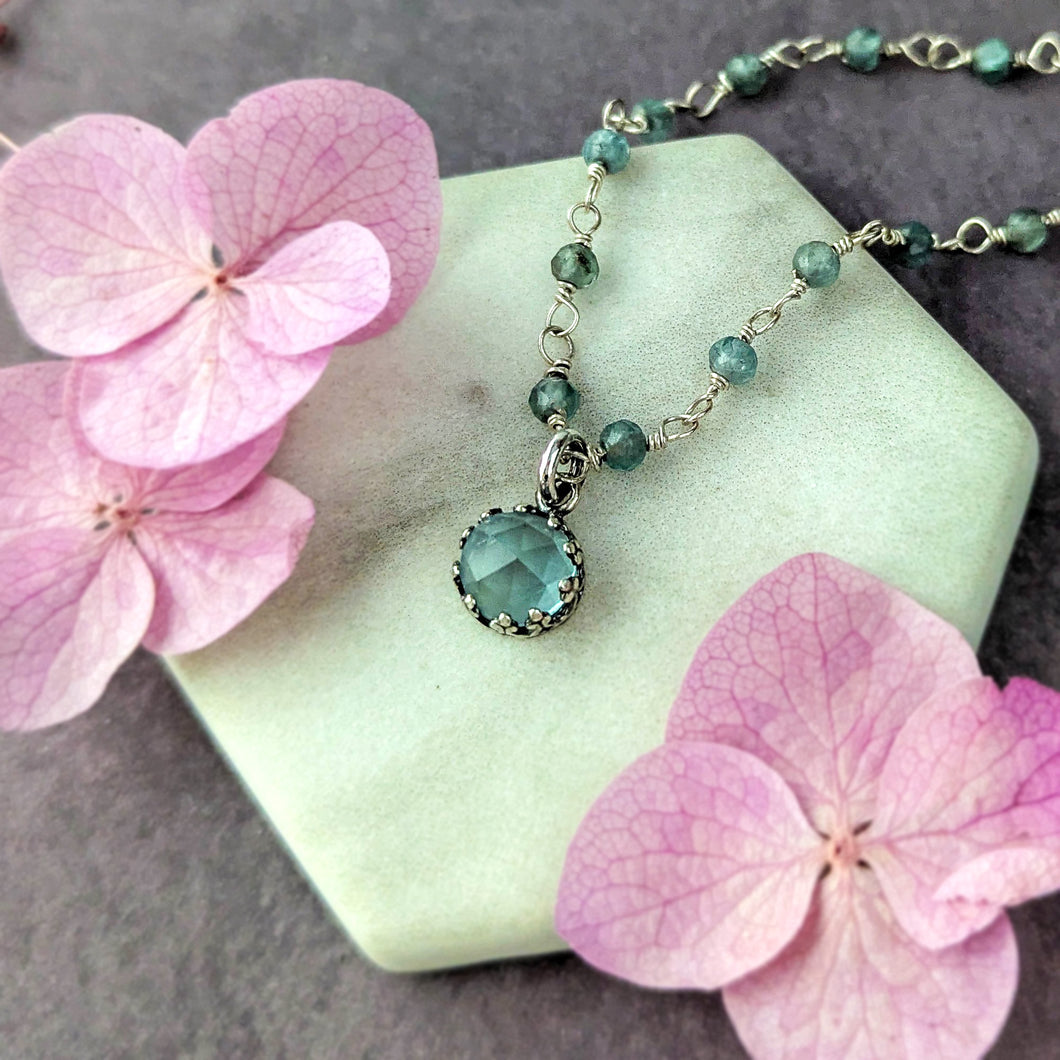 Necklace with a blue pendant on a white stone surrounded by pink flowers